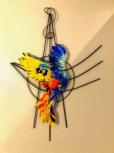 Parrot in Flight: a yellow, blue, and red fused-glass parrot in flight, on a black wrought-iron armature.