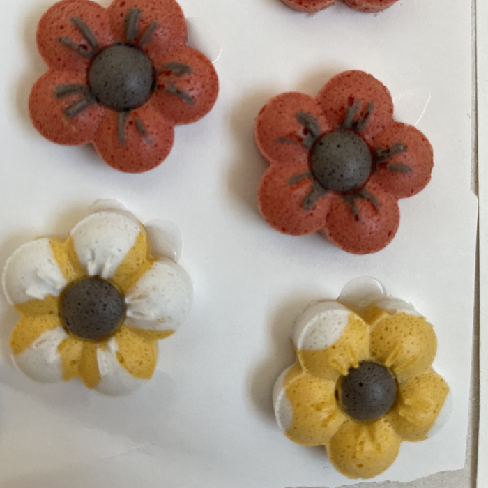 Fake Freeze and Fuse free tutorial cover: four little flowers made of powdered frit and layering mix, two rust red and two yellow and white, each with a dark center, dried and ready for the kiln.