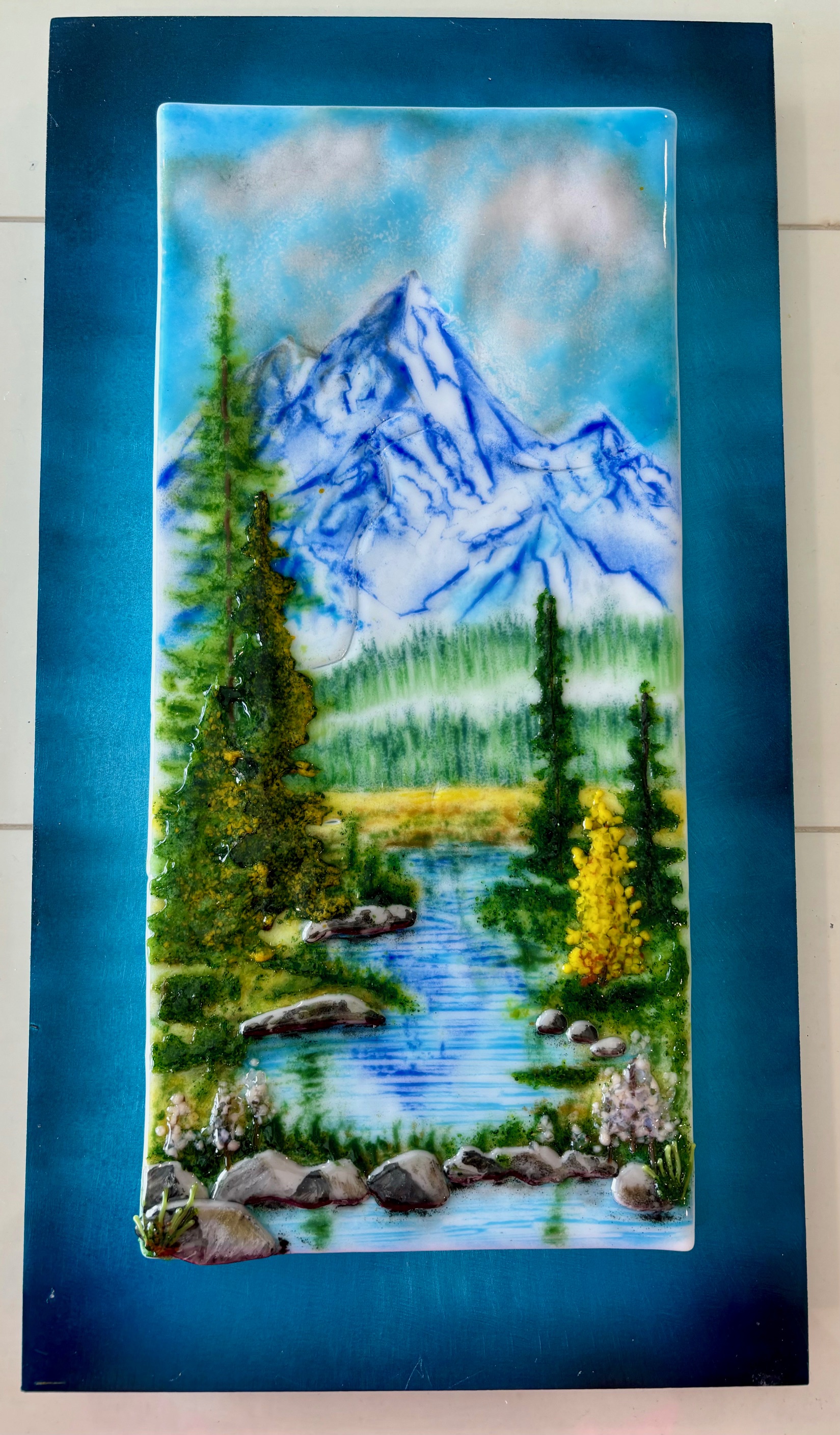 Fused-glass panel of a mountain stream running through evergreens.